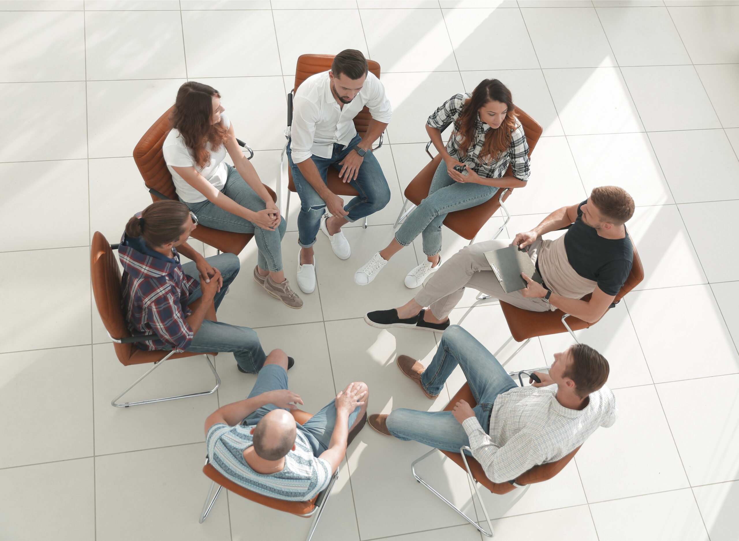 shutterstock_1125297071 Foto Av flere mennesker som sitter på stoler plassert i ring